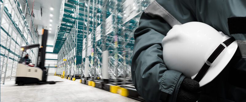 Commercial Casualty Insurance - Warehouse worker holding white hard hat with forklift in background