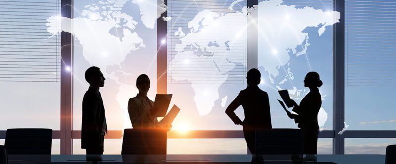 International Insurance Programs - Image of Silhouette of business people in meeting room in front of world map